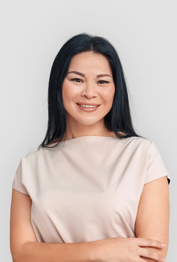 A portrait of a smiling middle-aged woman with dark hair and a neutral-toned top, representing a satisfied patient or a healthy, natural aesthetic.