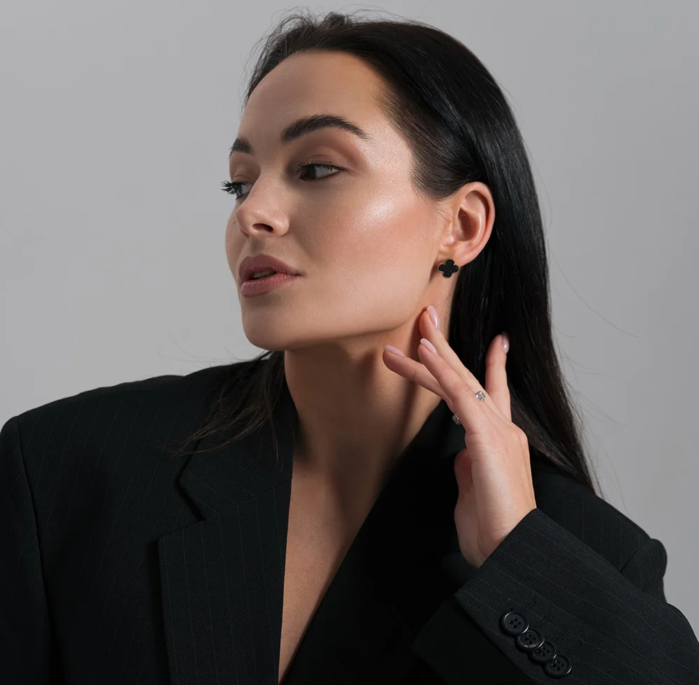 A beautiful woman with long, dark hair, wearing a black pinstripe blazer. She is looking to her left, with her left hand near her neck. She is wearing small black stud earrings and a ring with a small stone on her left hand. The background is a solid, light gray. - Exosomes in Draper, UT